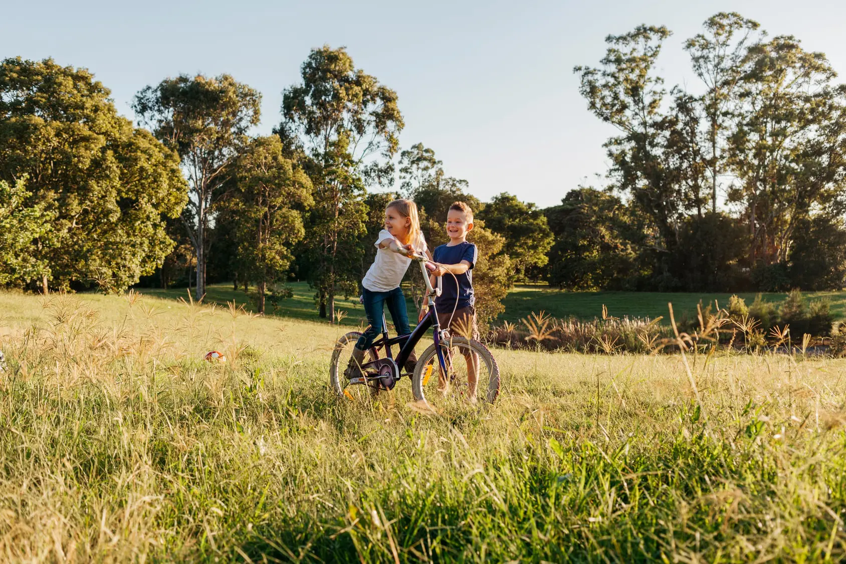 Two young children riding bike in park
